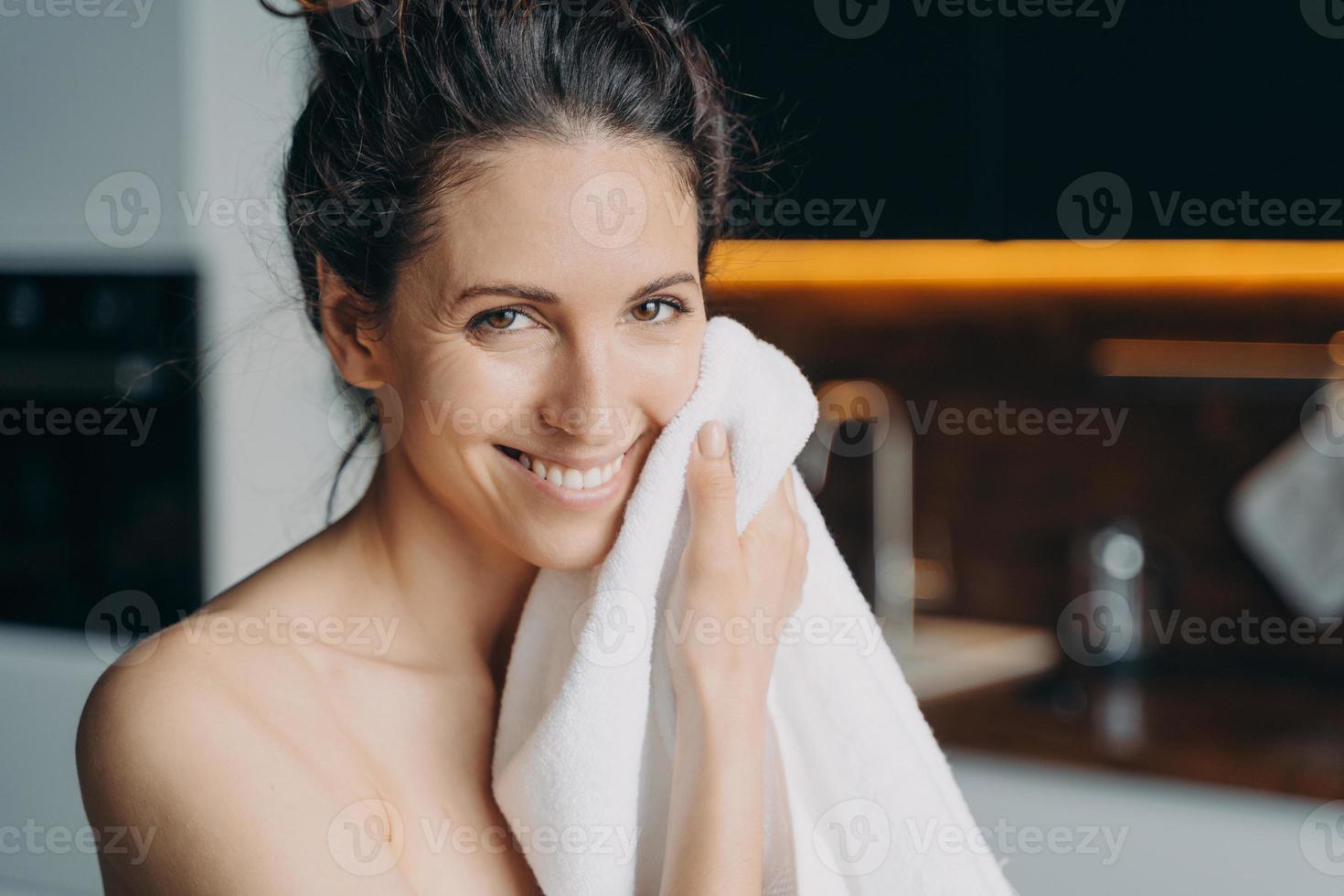 kaukasische vrouw veegt gezicht af met een handdoek en glimlacht. hygiëne, dermatologie en huidreiniging. foto