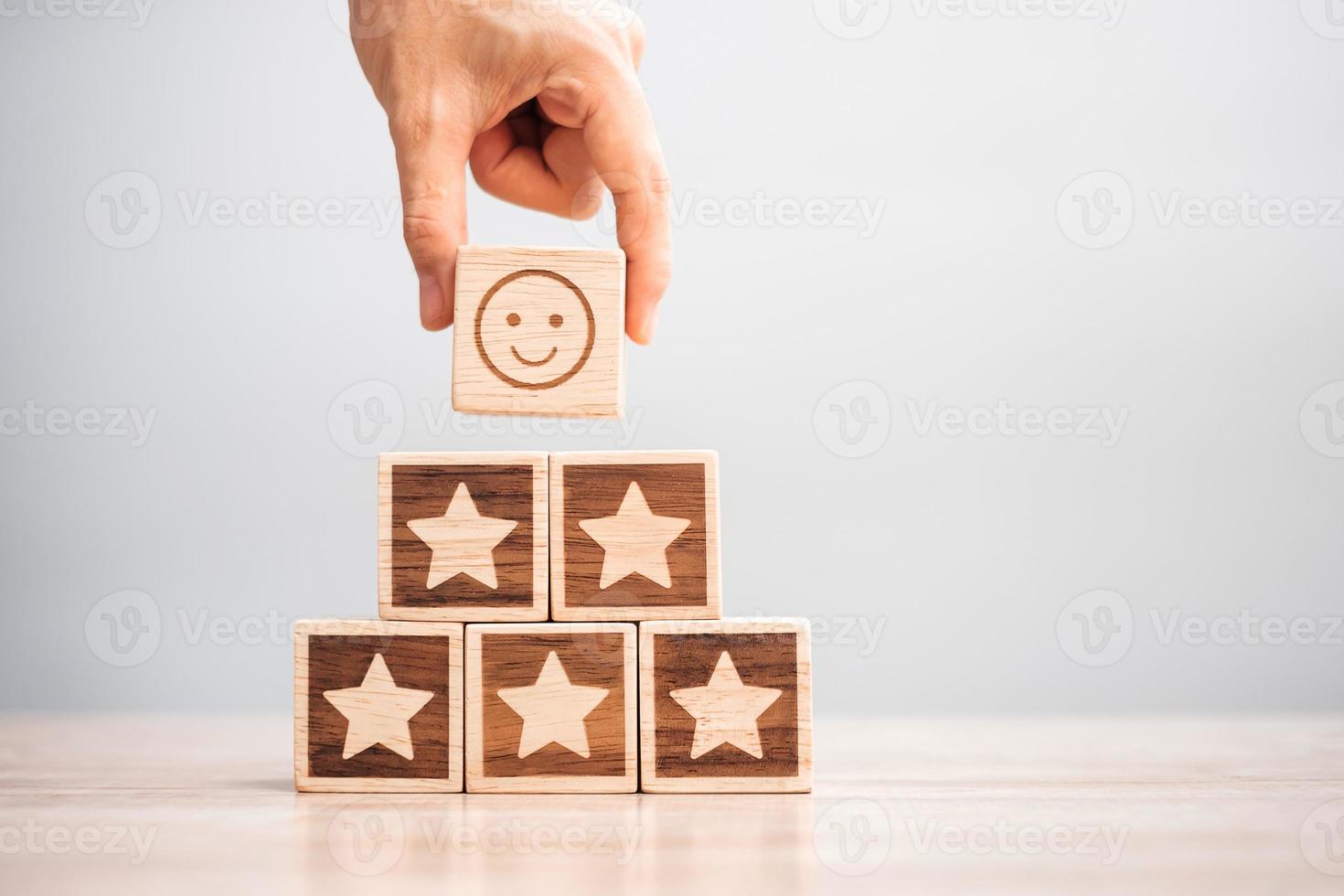 hand met glimlach gezicht over ster symbool blokken op tafel achtergrond. servicebeoordeling, rangschikking, klantbeoordeling, tevredenheid, evaluatie en feedbackconcept foto