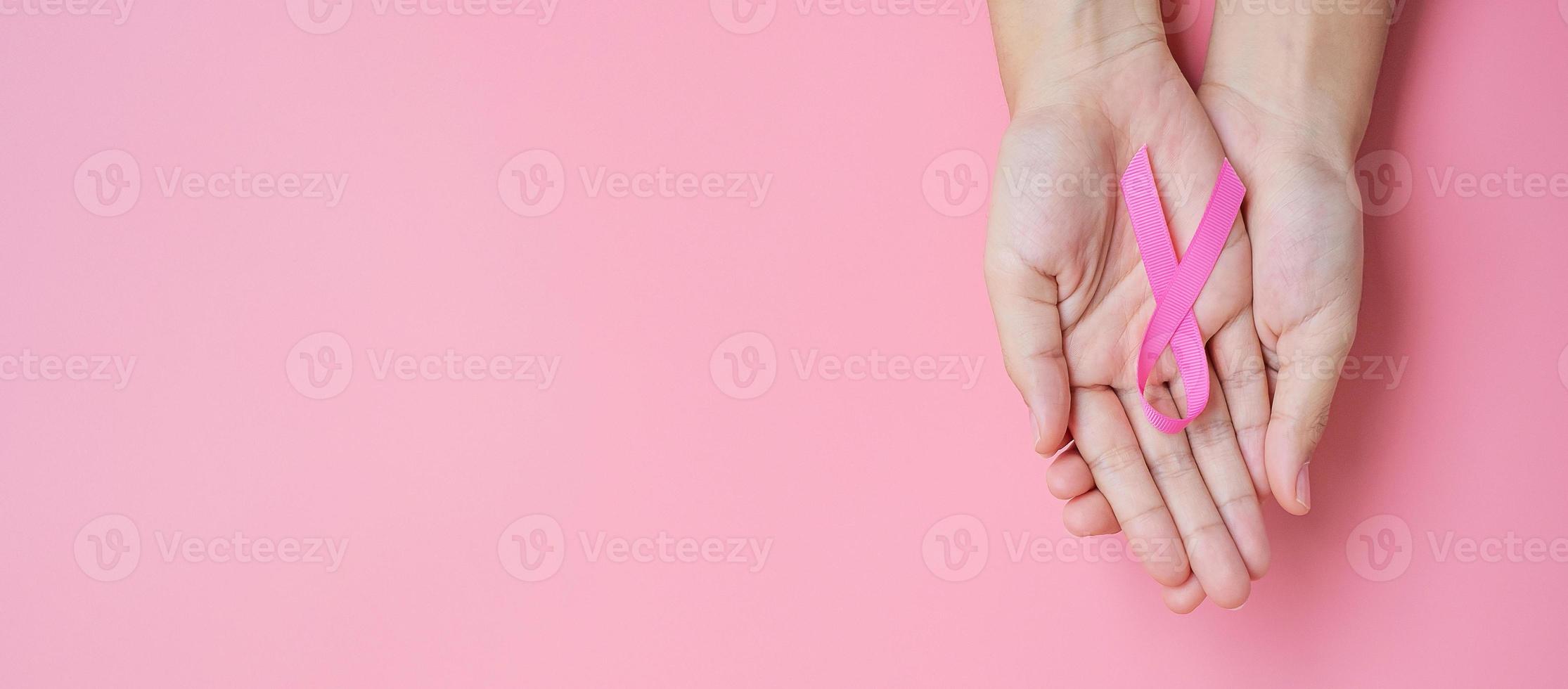 oktober borstkanker bewustzijn maand, volwassen vrouw hand met roze lint op roze achtergrond voor het ondersteunen van mensen die leven en ziekte. internationaal vrouwen-, moeder- en wereldkankerdagconcept foto