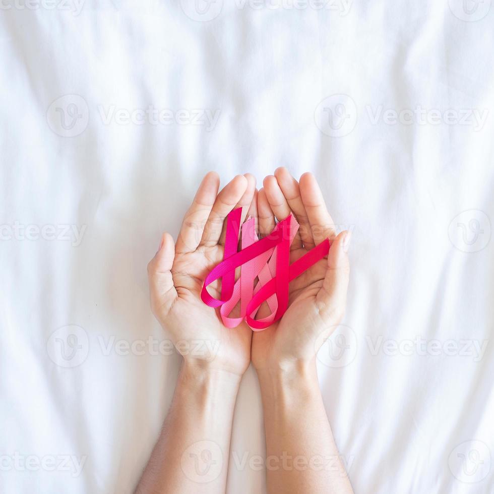 oktober borstkanker bewustzijn maand, volwassen vrouw hand met roze lint op roze achtergrond voor het ondersteunen van mensen die leven en ziekte. internationaal vrouwen-, moeder- en wereldkankerdagconcept foto