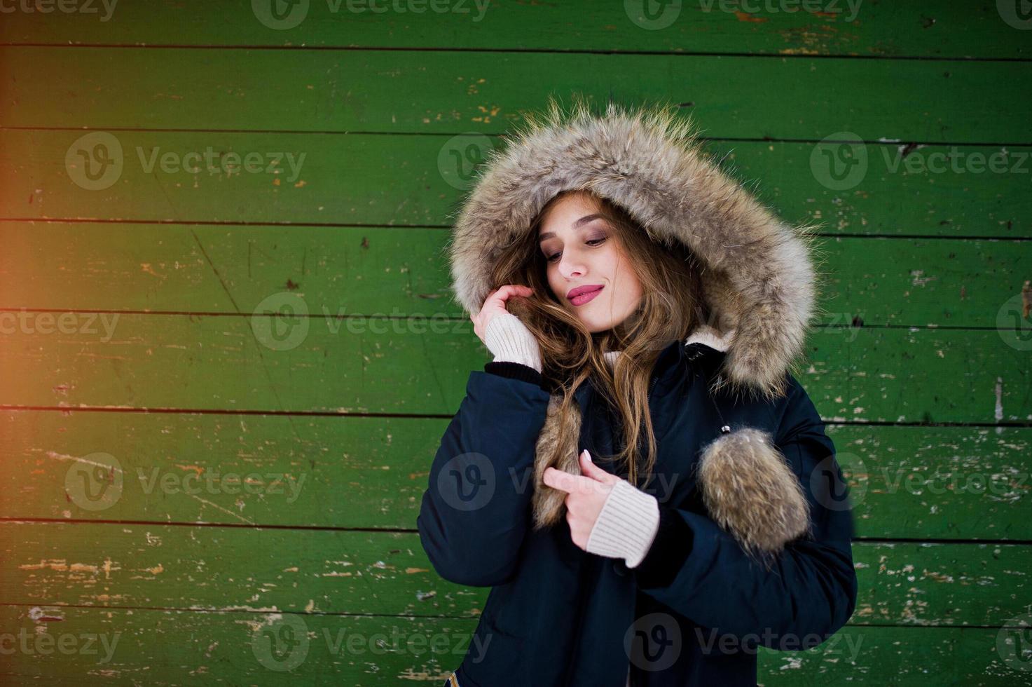 mooie brunette meisje in warme winterkleding. model op winterjas tegen groene houten achtergrond. foto