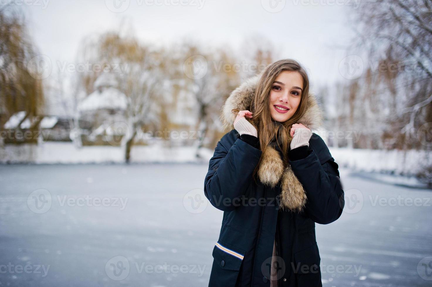 mooie brunette meisje in warme winterkleding. model op winterjas tegen bevroren meer in het park. foto