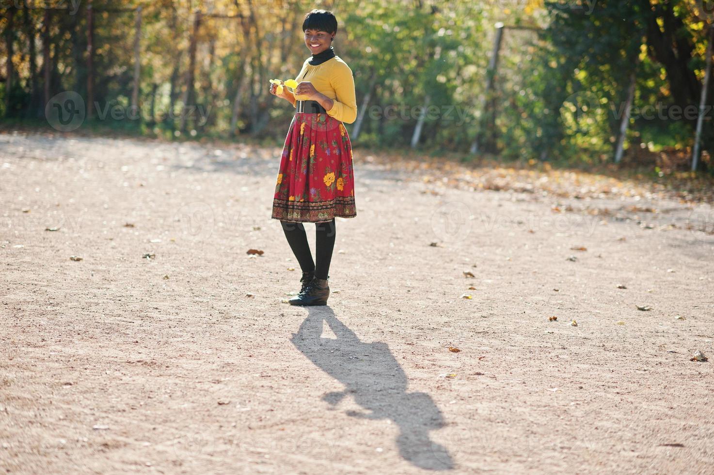 Afrikaans Amerikaans meisje bij gele en rode jurk in het gouden herfstpark. foto