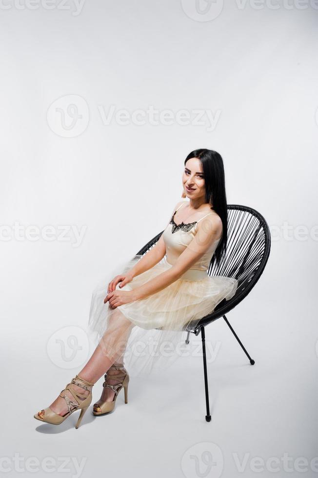 portret van brunette meisje op beige jurk met stoel geïsoleerd op wit. foto