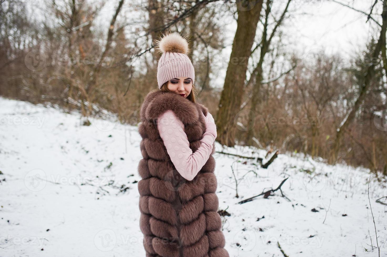 stijlvol meisje in bontjas en hoofddeksels in het winterbos. foto