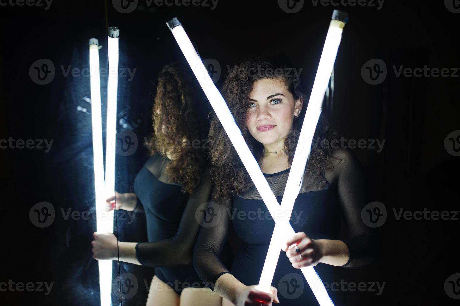 krullend brunette plus size model met twee lange led-lampen in de dansruimte met spiegel. foto