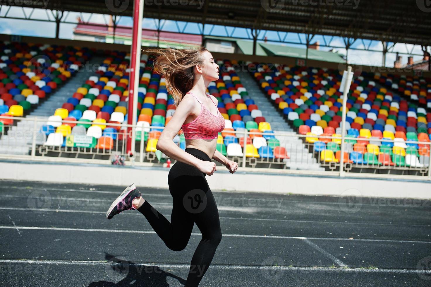 fitness sportief meisje in sportkleding bij stadion buitensporten. gelukkig sexy vrouw draait op atletische baan loopband op stadion. foto