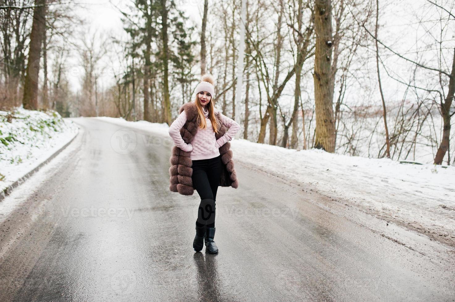 stijlvol meisje in bontjas en hoofddeksels op winterdag op weg. foto
