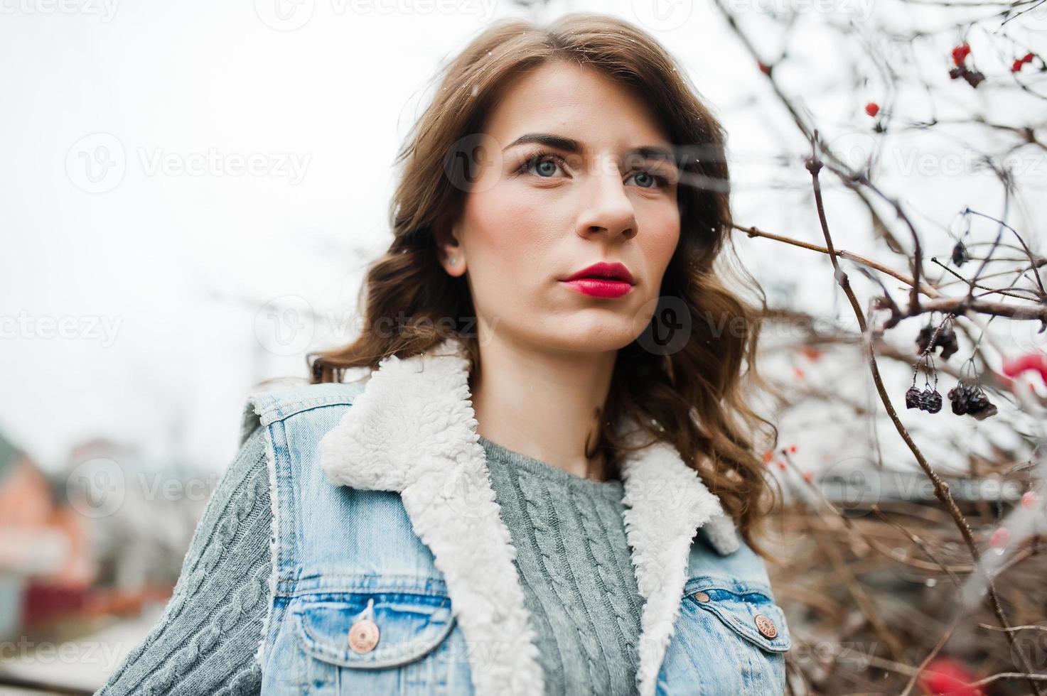portret van brunette meisje in jeans jasje bij bevroren struiken. foto