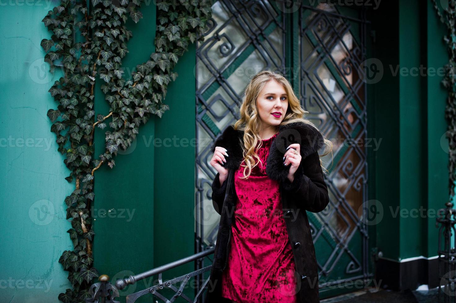 elegantie blond meisje in rode avondjurk en bontjas in de straten van de stad. foto