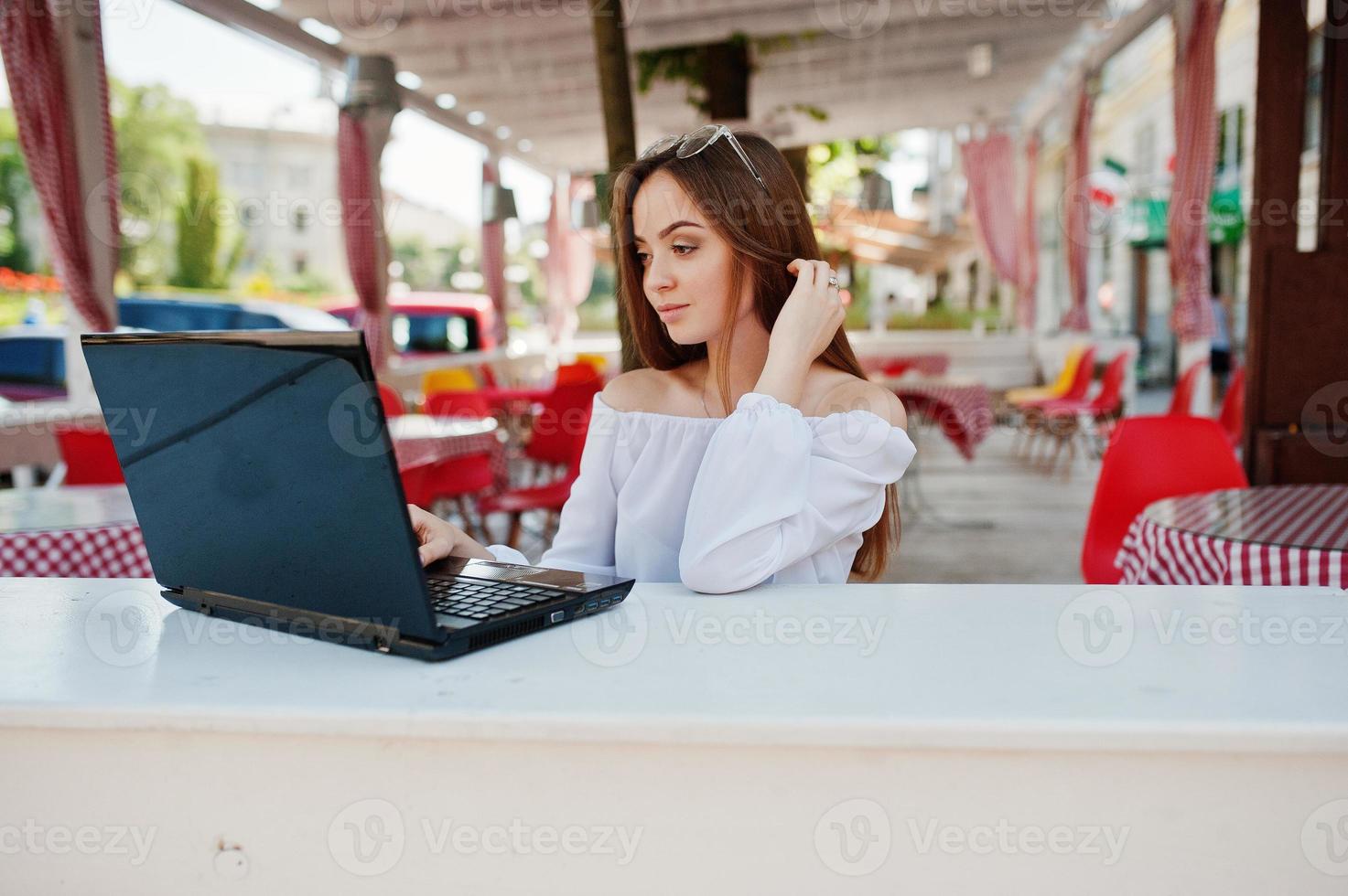 portret van een sterke onafhankelijke succesvolle zakenvrouw die slimme vrijetijdskleding en een bril draagt en op een laptop in een café werkt. foto