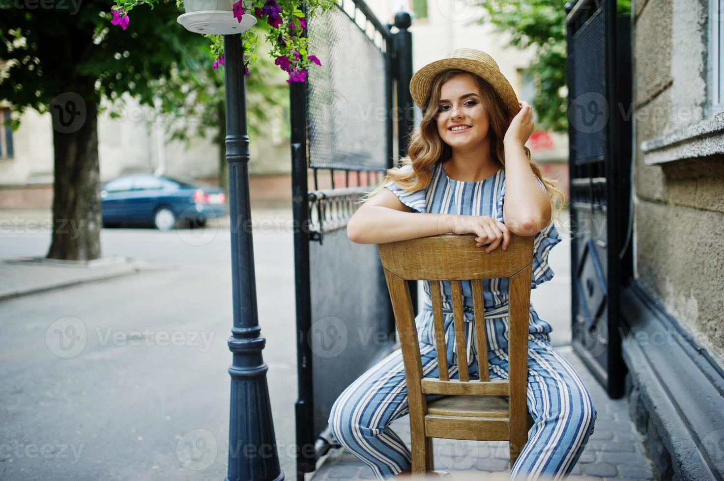 portret van een fantastische jonge vrouw in gestreepte overall en hoed zittend en poserend op de stoel buiten. foto