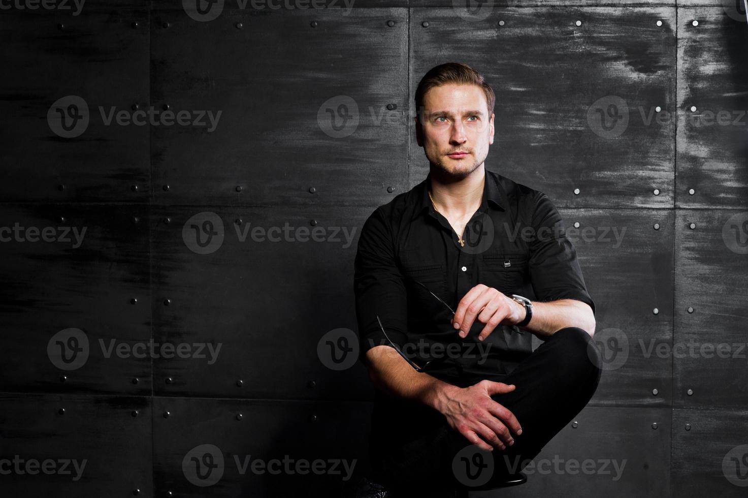 studio portret van stijlvolle man slijtage op zwart shirt tegen stalen muur. foto