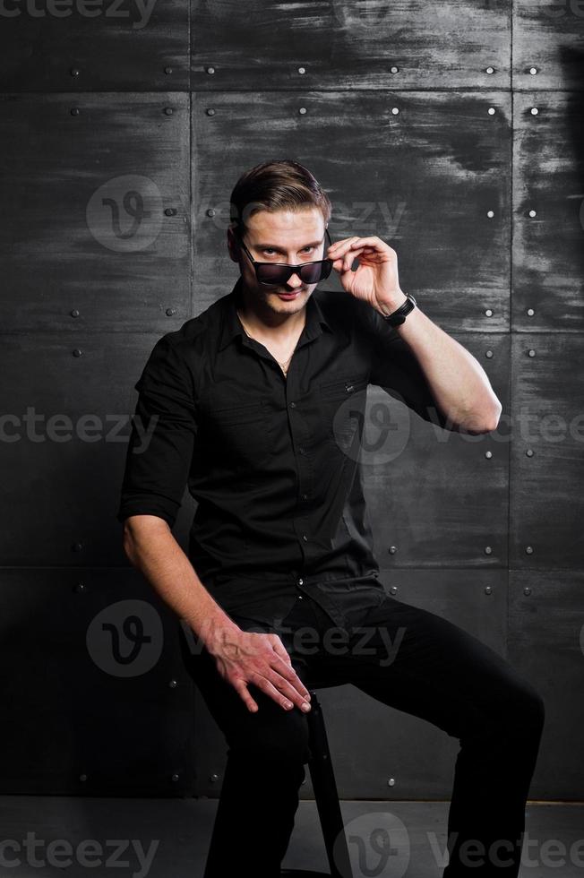 studio portret van stijlvolle man slijtage op zwart shirt en bril tegen stalen wand. foto