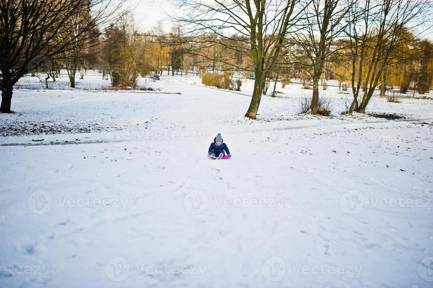 schattig klein meisje met schotel sleeën buiten op winterdag. foto