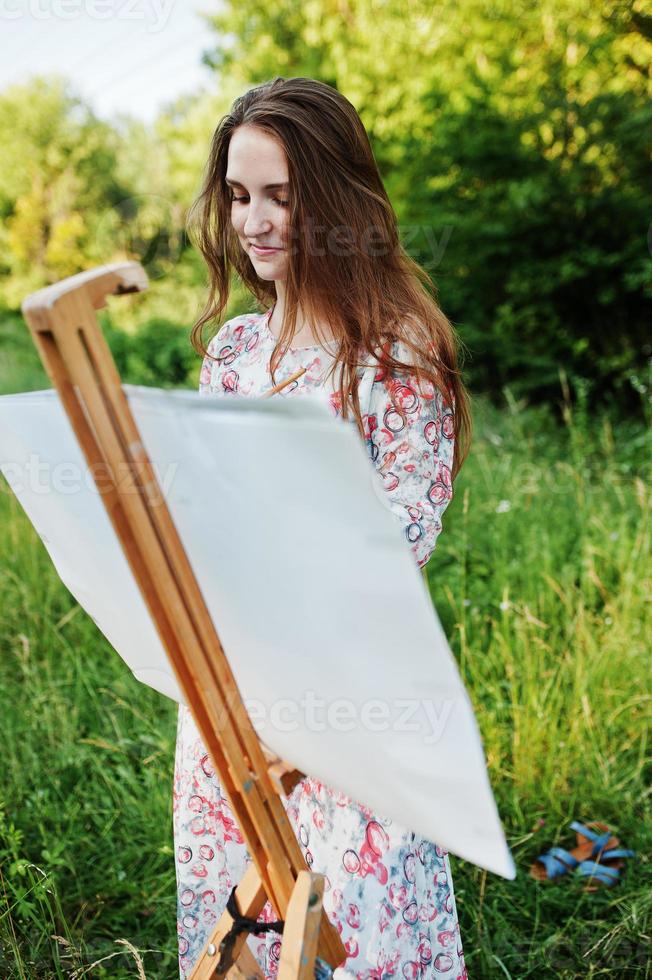 portret van een aantrekkelijke jonge vrouw in lange jurk schilderen met waterverf in de natuur. foto