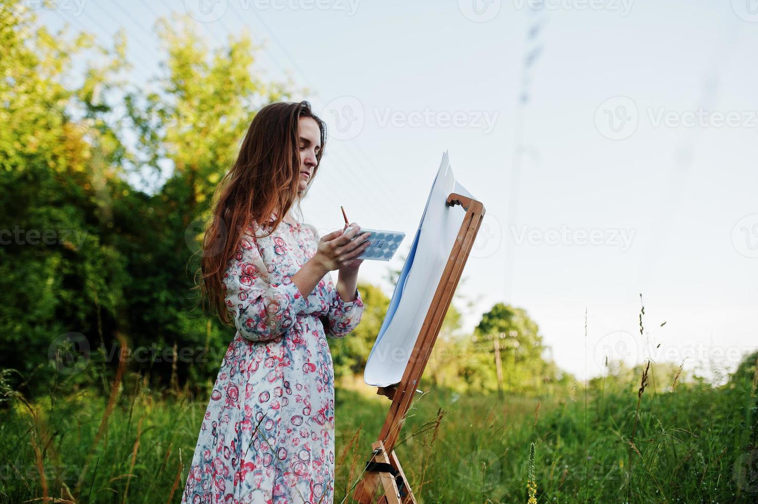 portret van een aantrekkelijke jonge vrouw in lange jurk schilderen met waterverf in de natuur. foto