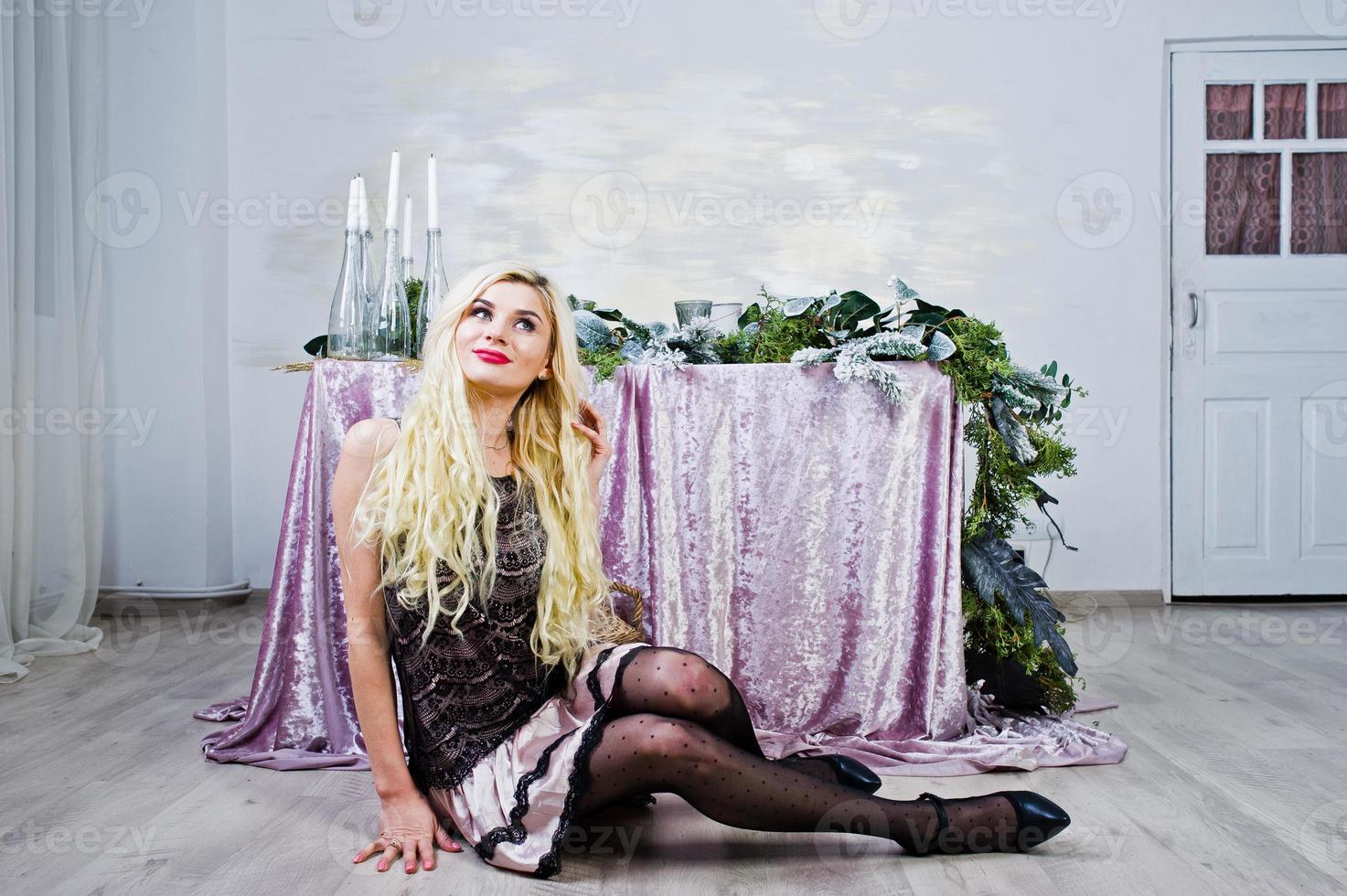Elegante blonde meid draagt een zwarte jurk die tegen een tafel zit met kerstversiering. foto