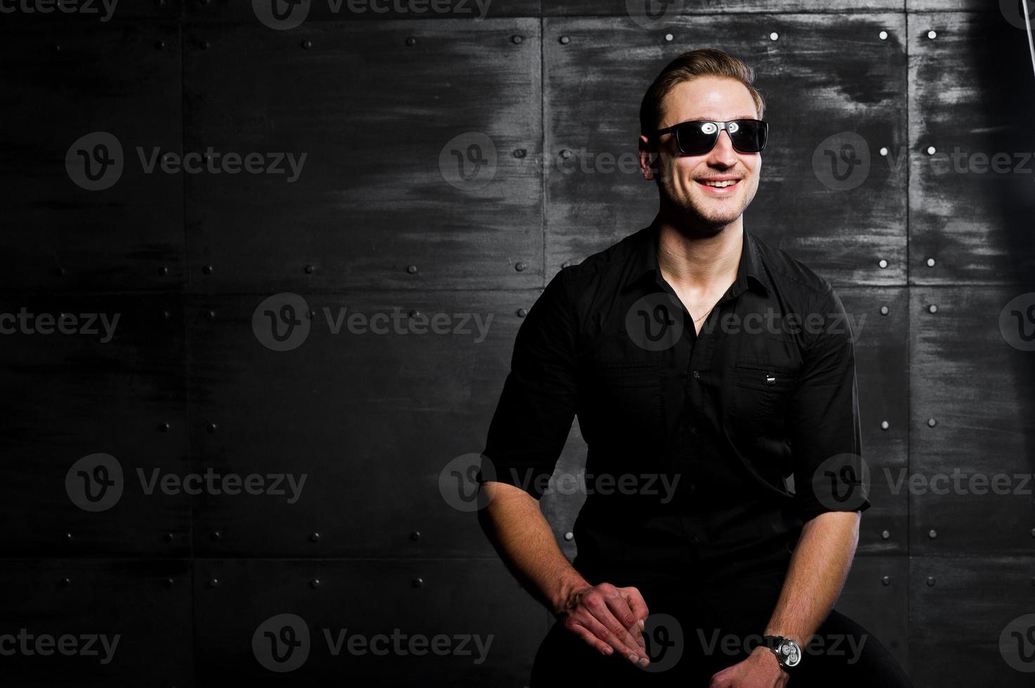 studio portret van stijlvolle man slijtage op zwart shirt en bril tegen stalen wand. foto