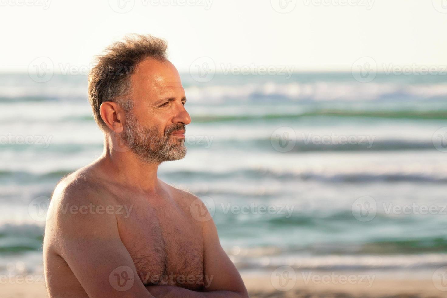 portret van een bebaarde shirtloze man in profiel op de zeeachtergrond in de zomerzonsondergang foto