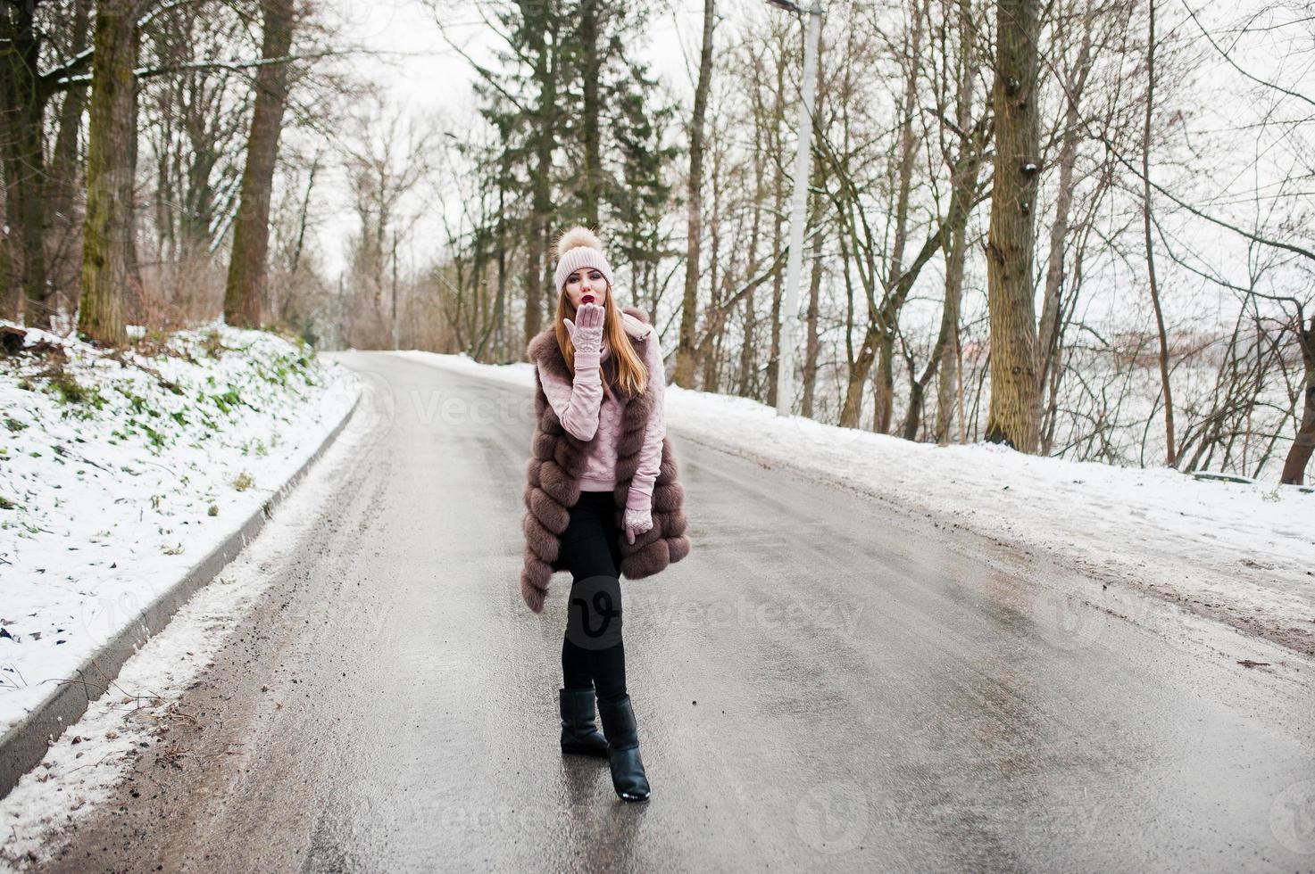 stijlvol meisje in bontjas en hoofddeksels op winterdag op weg. foto