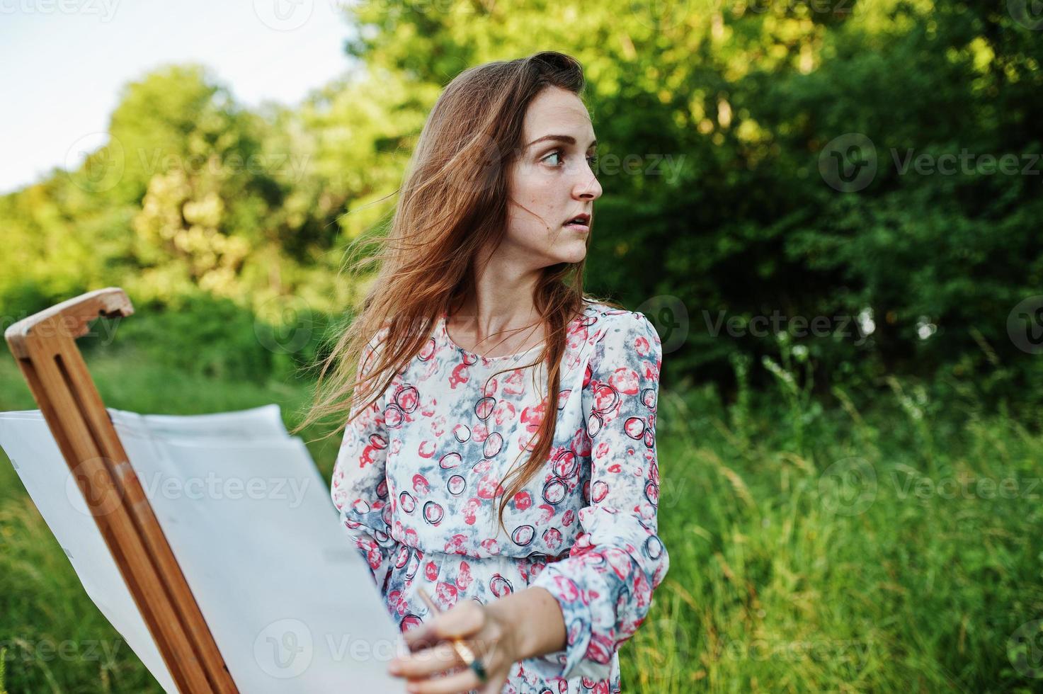 portret van een aantrekkelijke jonge vrouw in lange jurk schilderen met waterverf in de natuur. foto