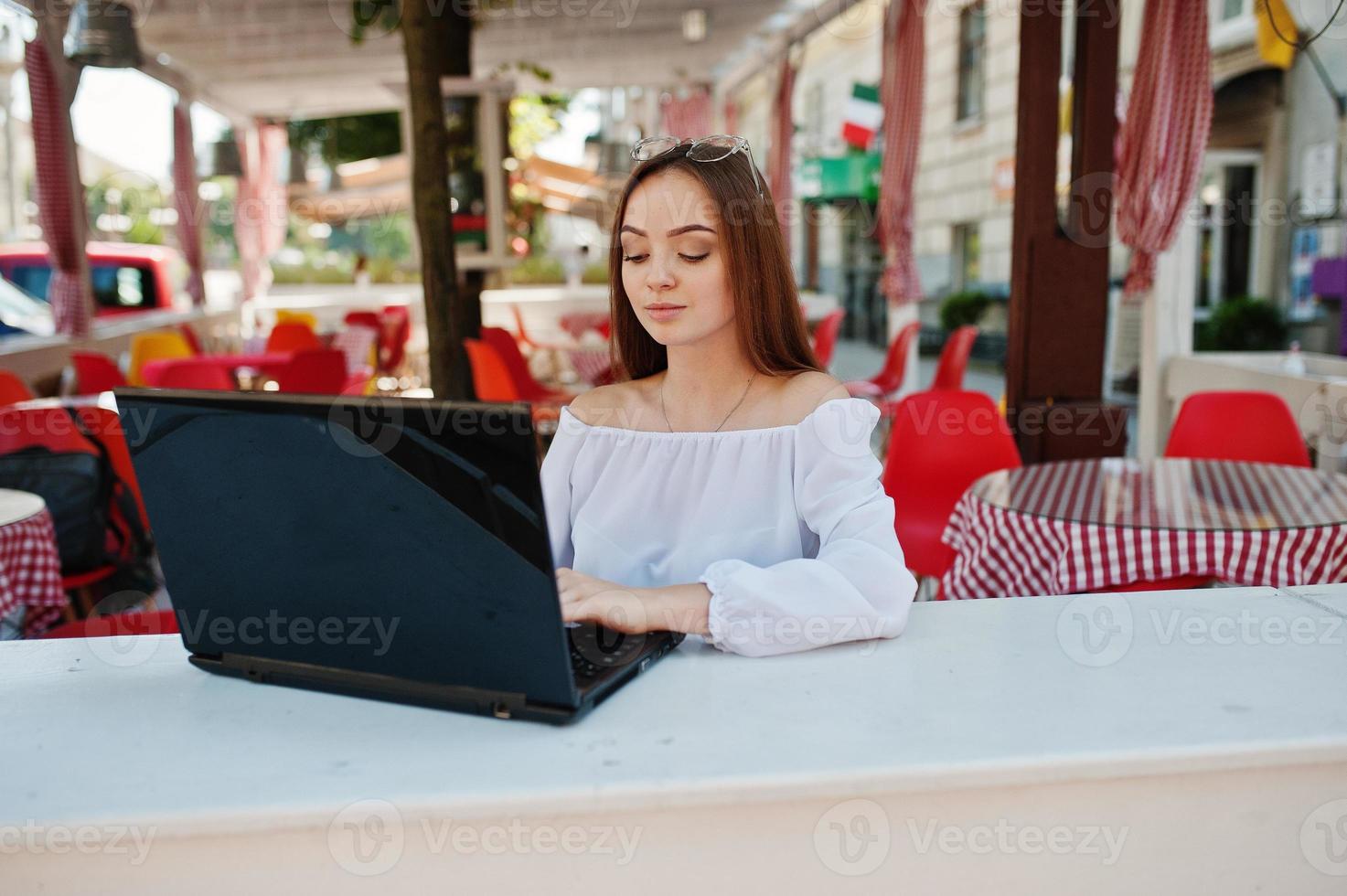 portret van een sterke onafhankelijke succesvolle zakenvrouw die slimme vrijetijdskleding en een bril draagt en op een laptop in een café werkt. foto