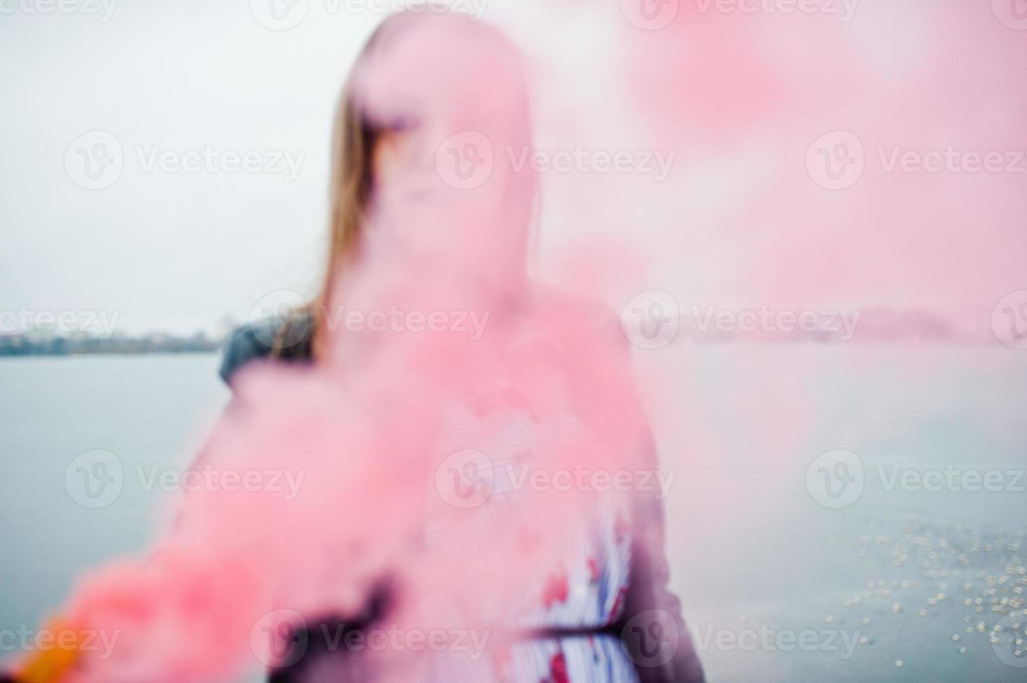 stijlvol meisje in leren jas houdt roze rookflare op winterdag tegen bevroren meer. foto