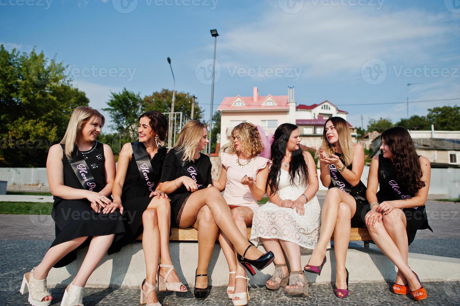 groep van 7 meisjes dragen op zwart en 2 bruiden die op de bank zitten en plezier hebben op vrijgezellenfeest. foto