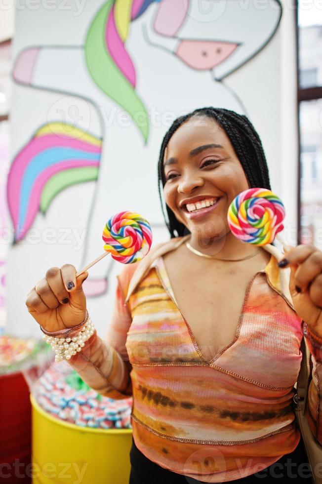 Afro-Amerikaanse duizendjarige dame bij snoepwinkel met lolipops. foto