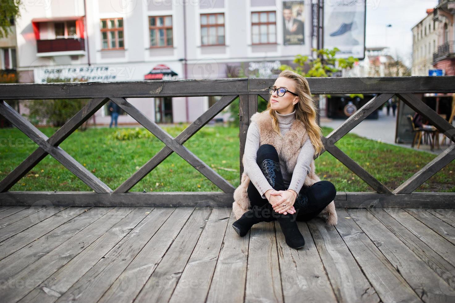 blond meisje op bontjas zittend op houten vloer buiten. foto