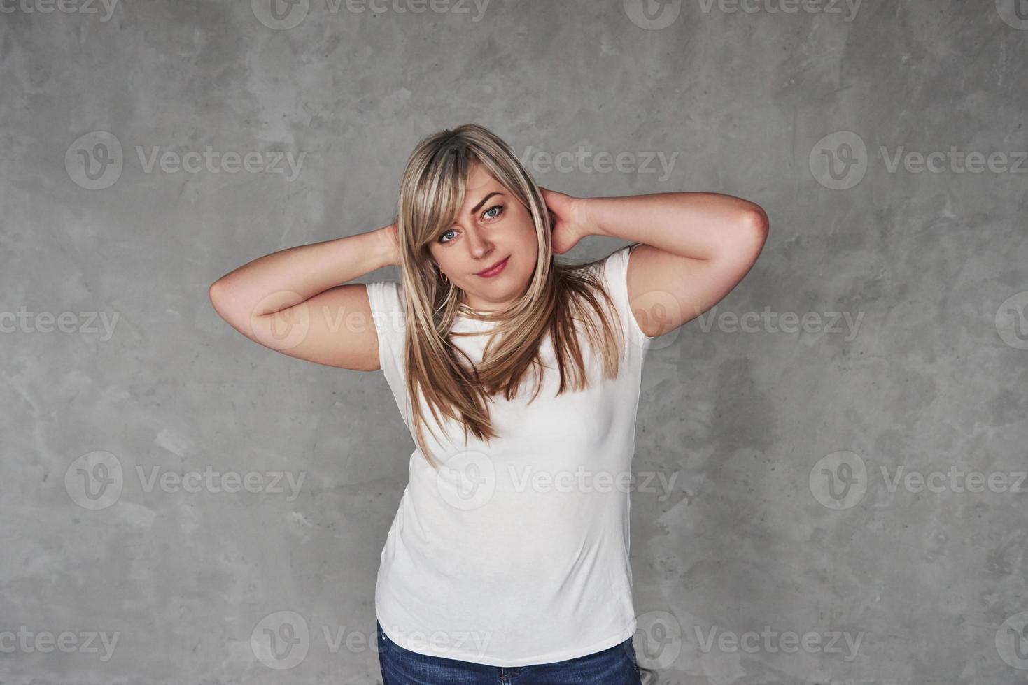 handen achter het hoofd. jonge blanke vrouw in de studio die tegen een grijze achtergrond staat foto