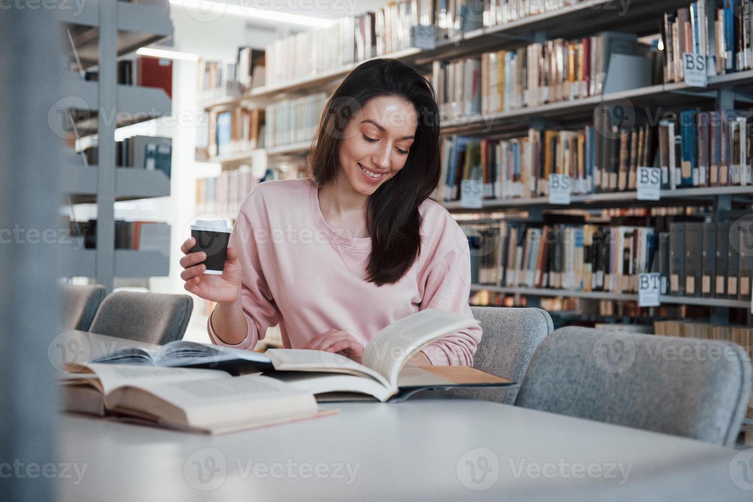 er is niemand die je zal storen. brunette meisje in vrijetijdskleding heeft plezier in de bibliotheek vol boeken foto