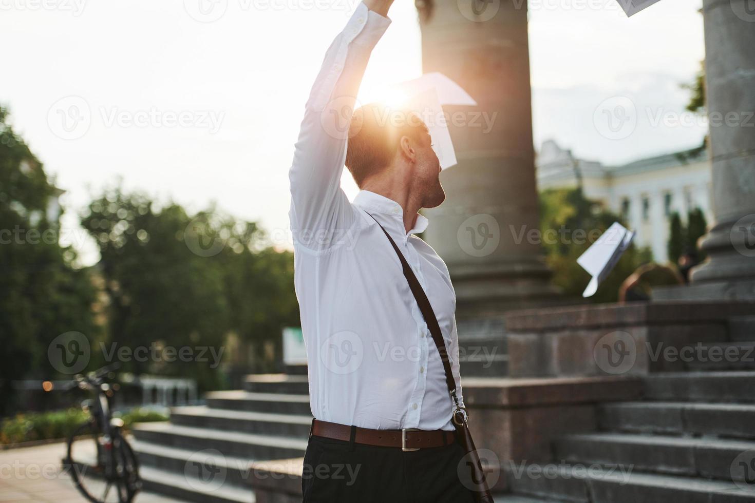 vellen papier in de lucht gooien. zakenman in formele kleding met zwarte fiets is in de stad foto