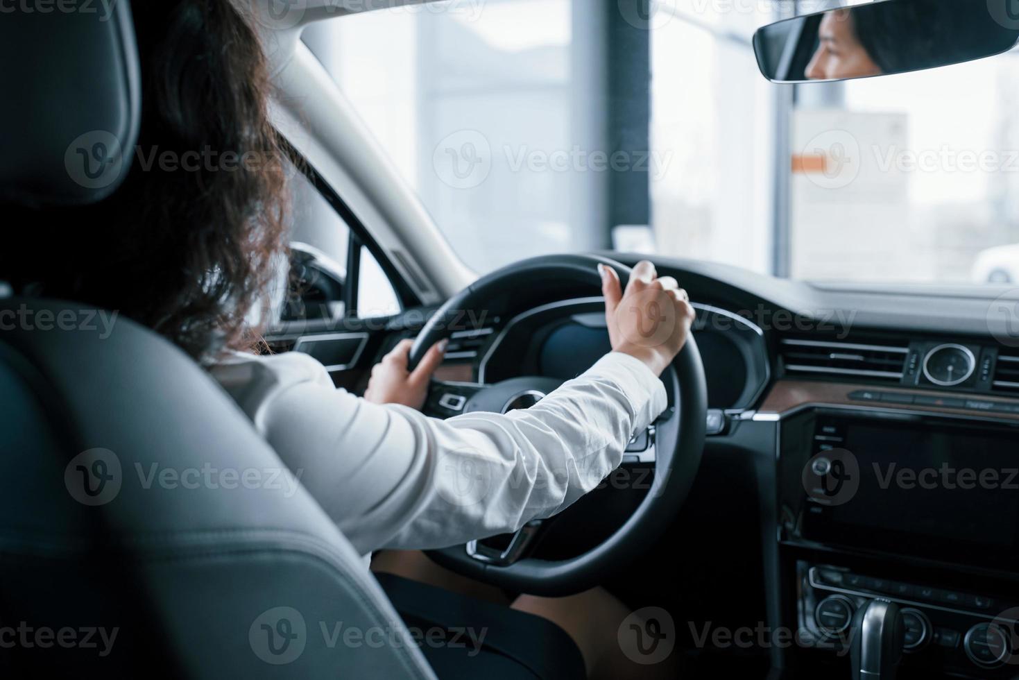 handen aan het stuur. mooie zakenvrouw probeert haar nieuwe auto in de autosalon foto