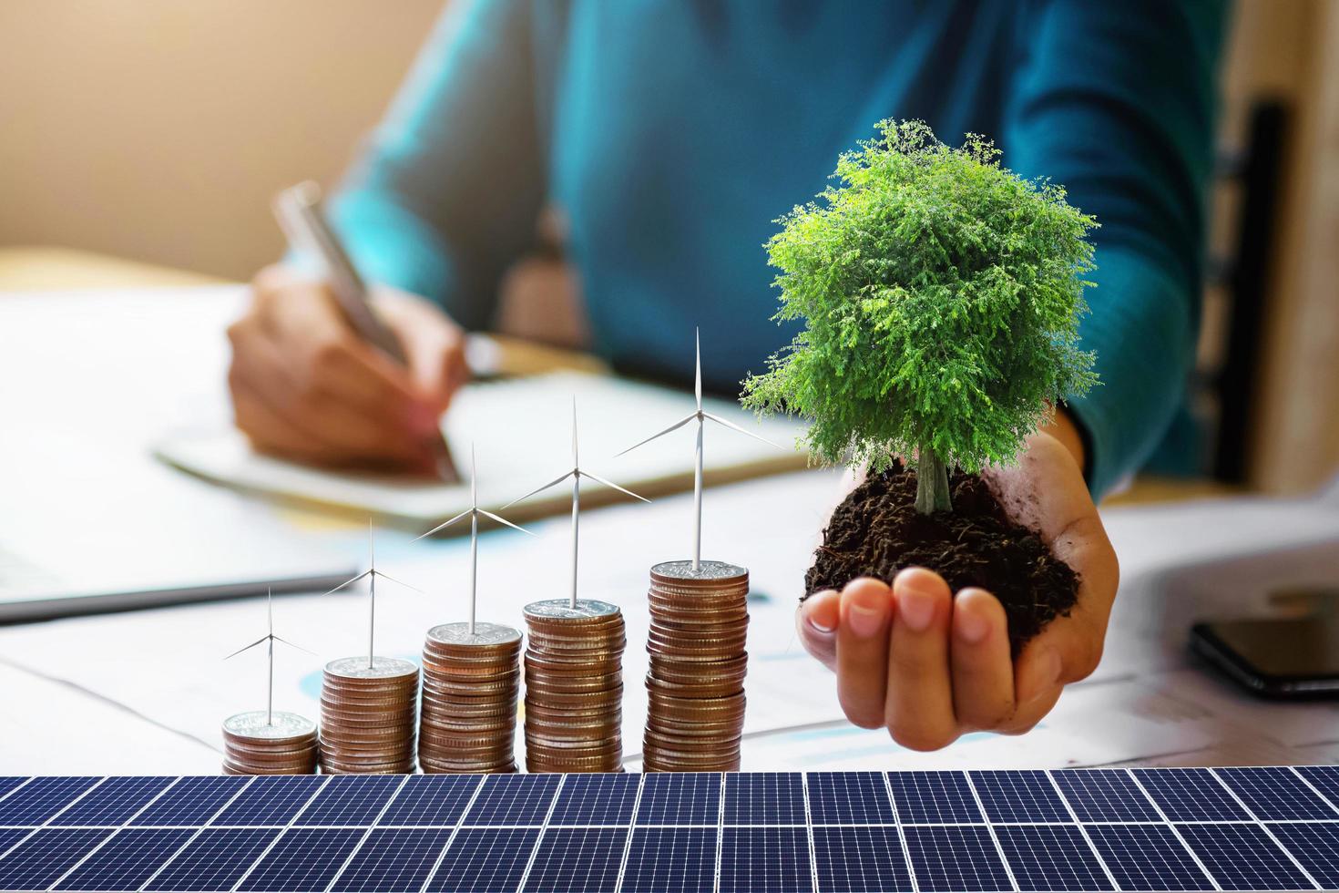 zakenvrouw met boom met turbine op munten en zonnepaneel. concept energie besparen en financiële boekhouding foto