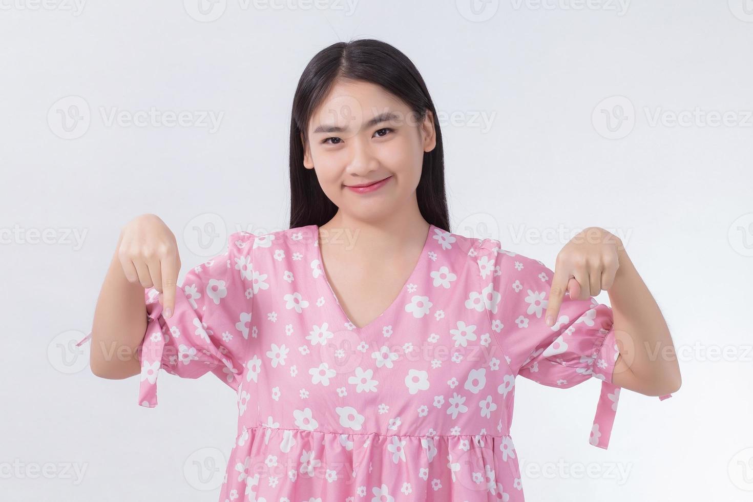 Aziatische mooie vrouw met zwart lang haar in roze shirt toont hand naar beneden om iets op een witte achtergrond te presenteren. foto