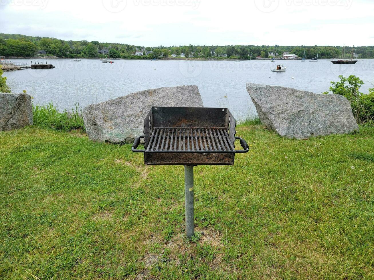 barbecuegrill in gras dichtbij meer met boten en rotsen foto