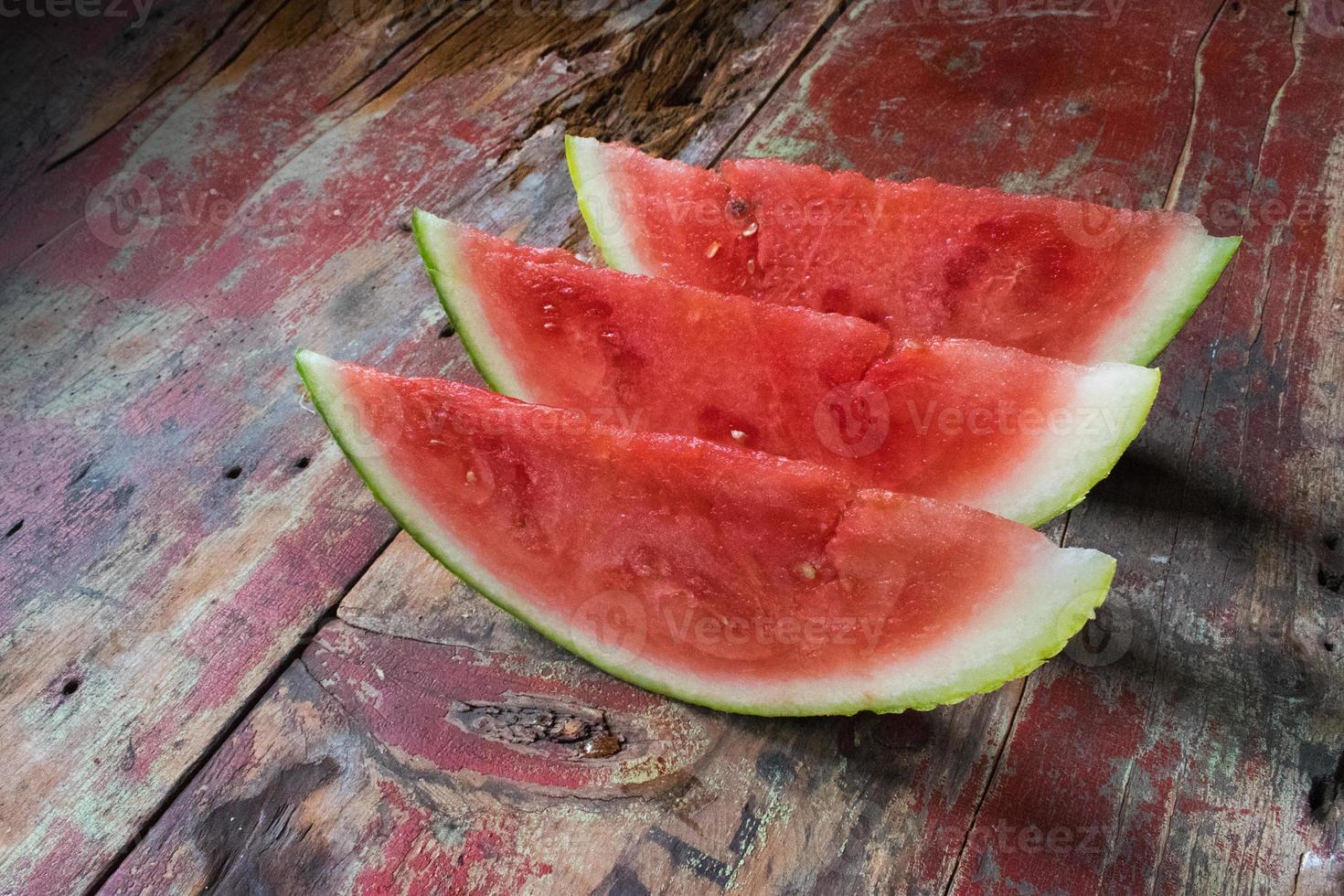 hele watermeloenplakken op een rij op een zijaanzicht van een rustieke houten tafel foto