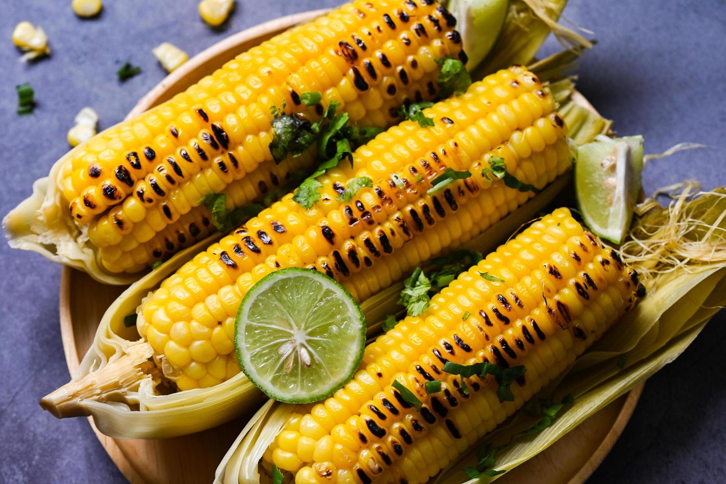 Suikermaïs eten met limoen en koriander, zoete maïs gekookt op plaat achtergrond, rijpe maïskolven gegrilde suikermaïs voor voedsel veganistisch diner of snack - bovenaanzicht foto