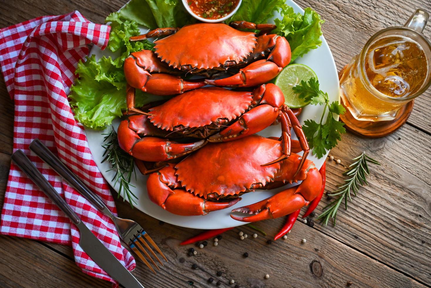 zeevruchten bord met kruiden specerijen rozemarijn citroen limoen salade sla groente, verse krab op witte plaat zeevruchten saus en mok bierglas, krab koken eten gekookt of gestoomd krab rood in het restaurant foto