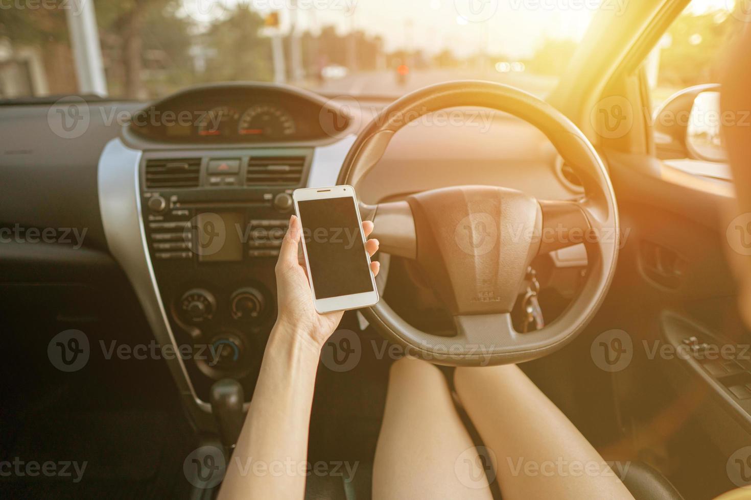 jonge vrouw in auto die haar smartphone controleert tijdens het rijden foto