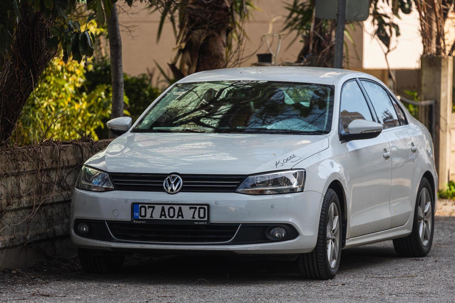 kant turkije 01 maart 2022 witte volkswagen jetta is geparkeerd op straat op een warme zomerdag tegen de achtergrond van een buildung, tuin foto