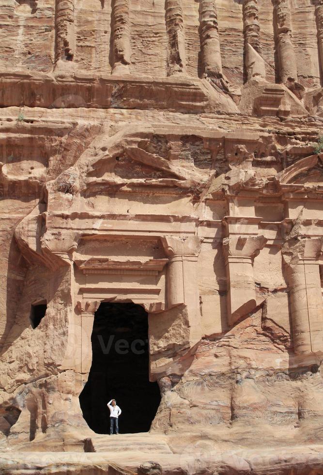 jonge man met een hoed in een monumentaal gebouw uitgehouwen in de rots in de oude jordaanse stad petra. foto