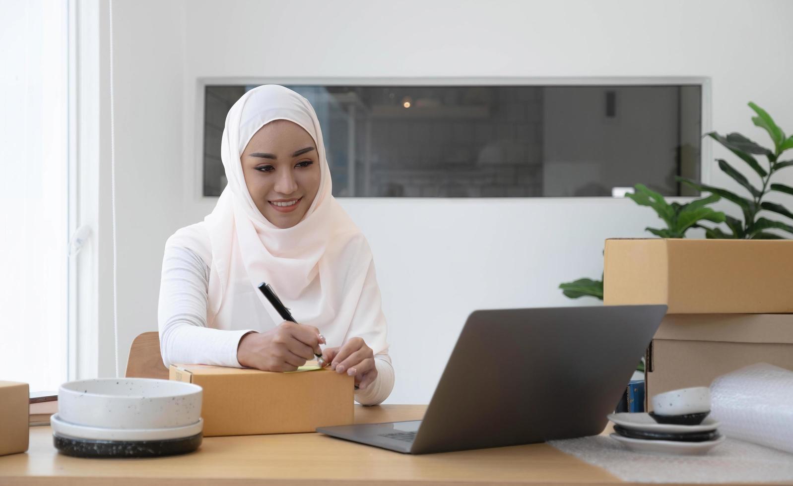 aantrekkelijke moslim vrouwelijke ondernemer, e-commerce ondernemer verpakking voorbereiding van een verzenddoos in haar kantoor. foto