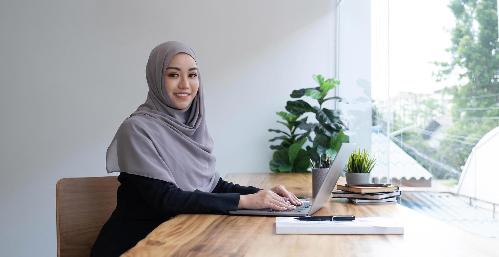 gelukkige Arabische vrouw freelancer chatten met klanten op laptop, zittend in café, lege ruimte foto