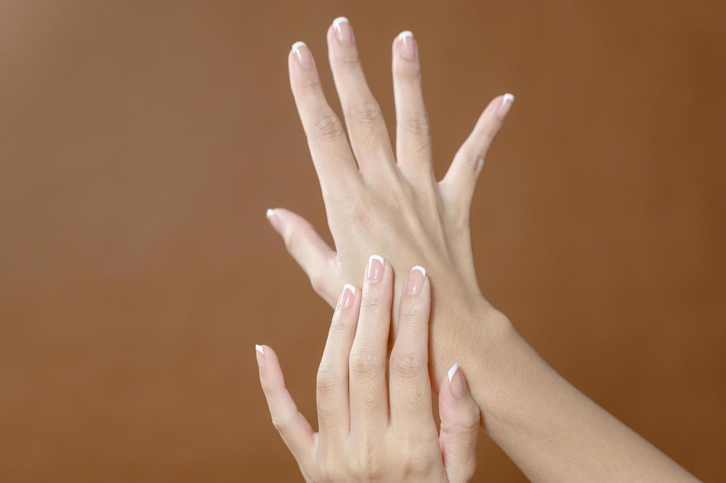 close-up jonge vrouwenhand brengt crème aan op bruine achtergrond, schoonheidshuidverzorgingsconcept foto