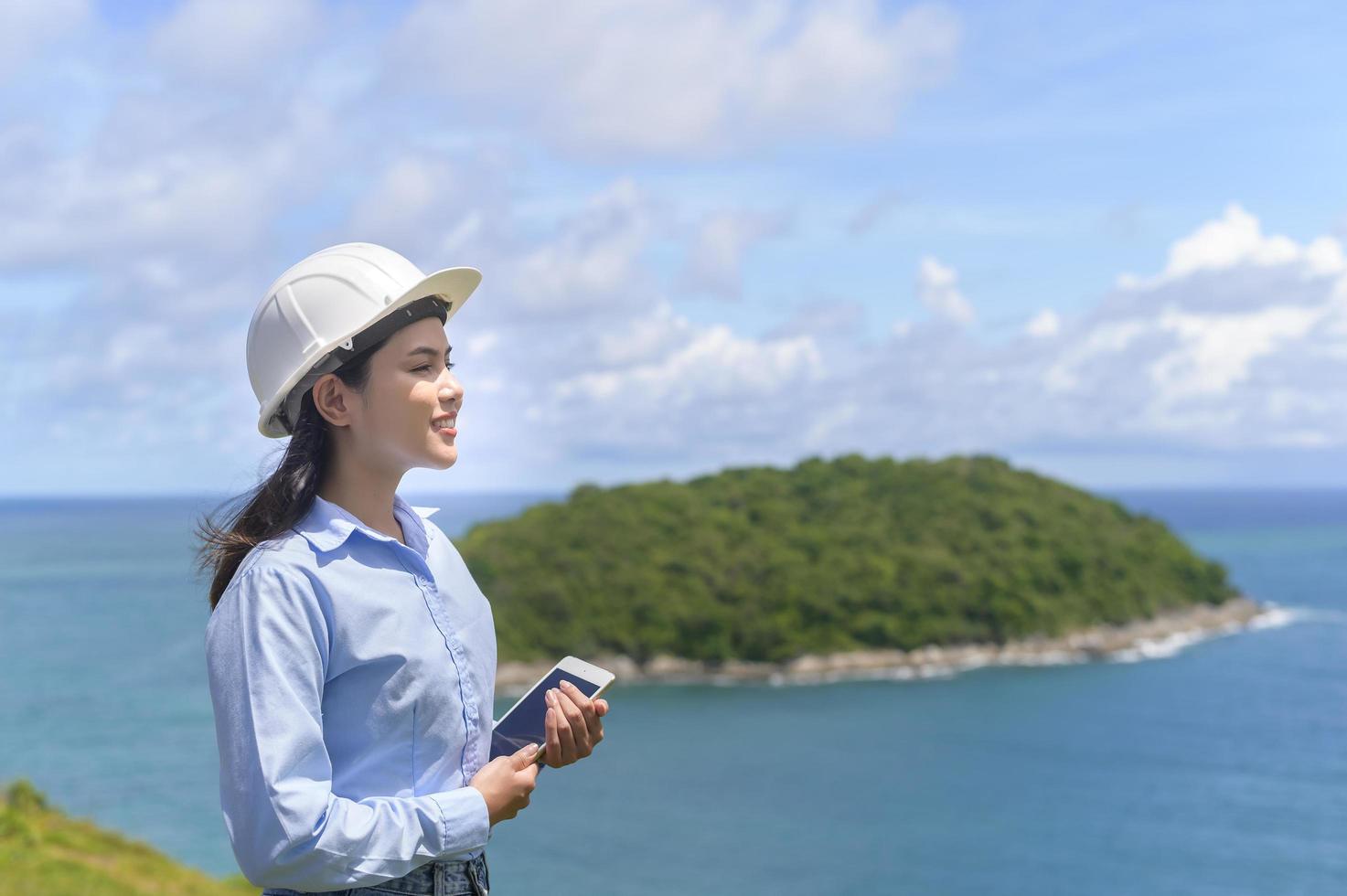 vrouwelijke ingenieur die aan de kust werkt en een beschermende helm draagt foto
