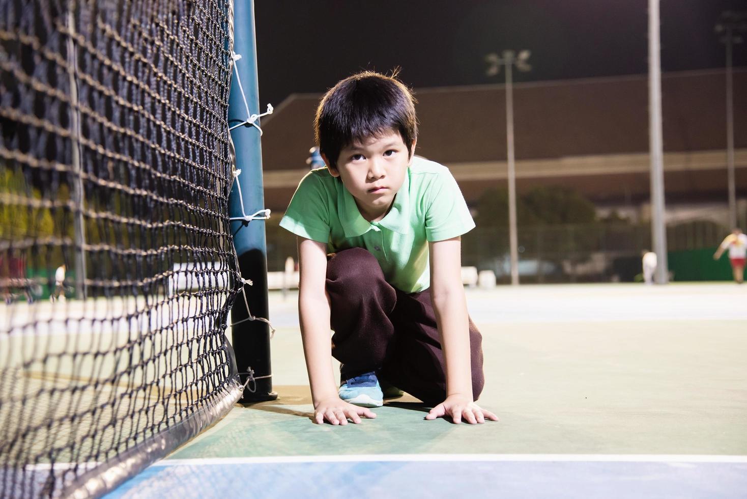 gelukkige jongen in tennisbaan tijdens zijn oefensporttijd - tennissport met mensenconcept foto