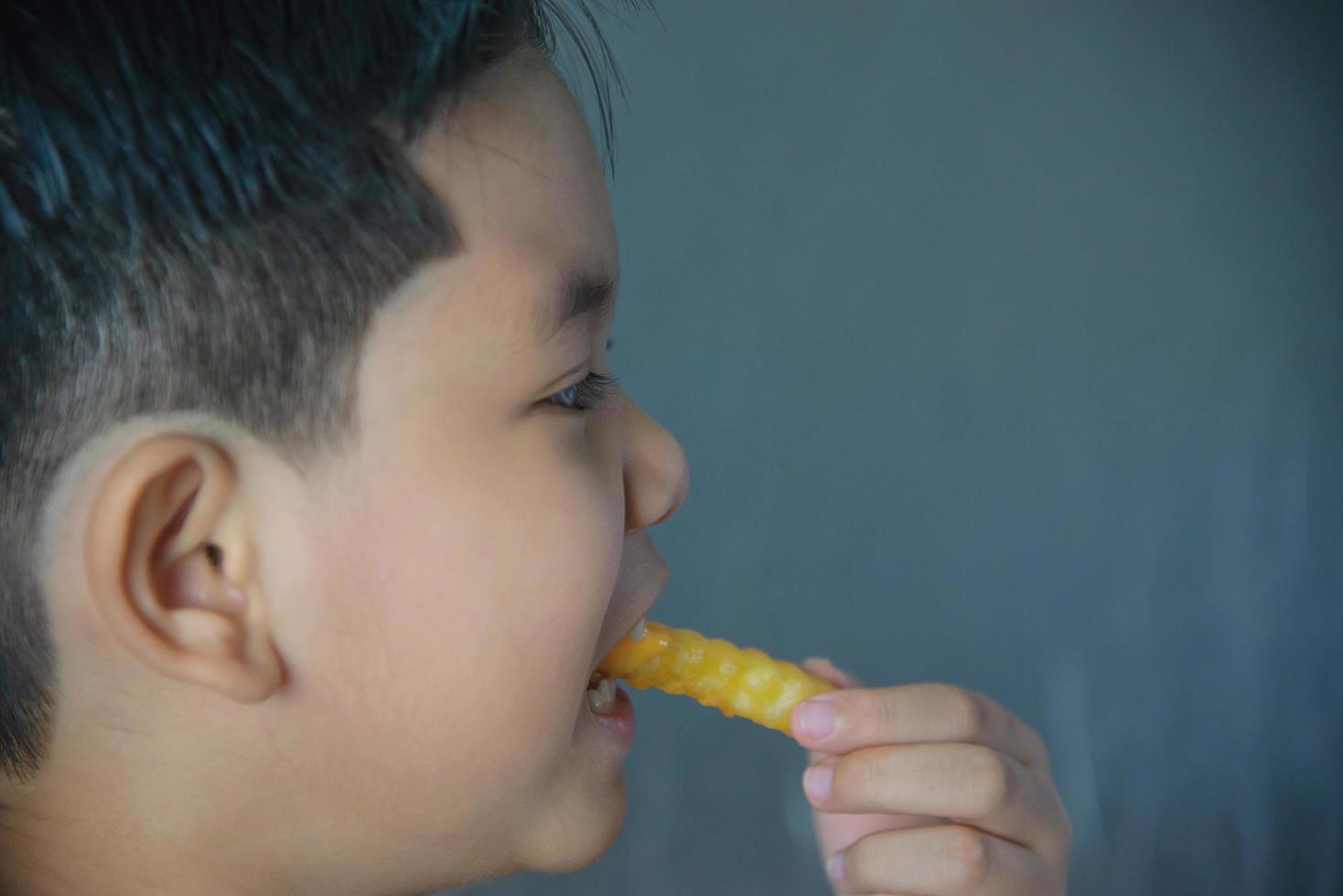 jongen die frietjesaardappel met gedimde saus eet over witte houten tafel foto
